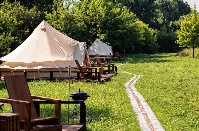 Tents with wooden chairs and pathway in front of them at glamping. Nature, greenery around